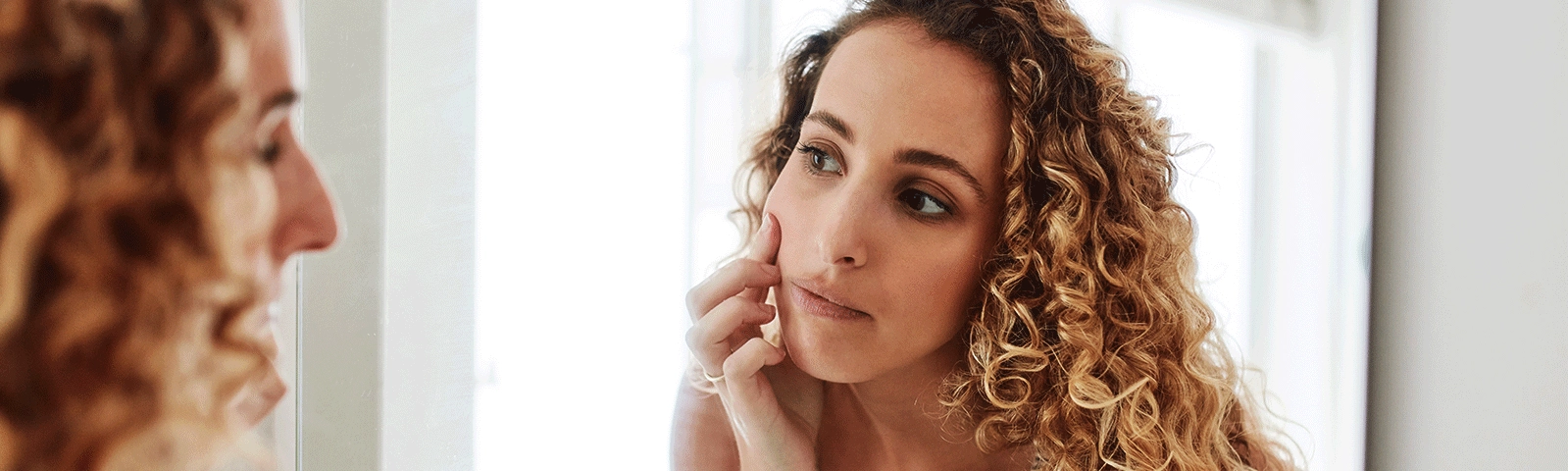 Woman looking in mirror at her skin