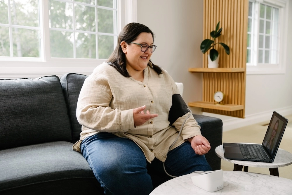 Woman sitting on couch taking blood pressure using virtual primary care