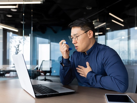 Man sitting at his work desk in office using his asthma inhaler.