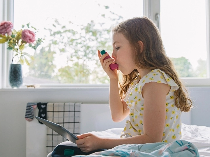Little girl sitting on bed using her asthma inhaler.