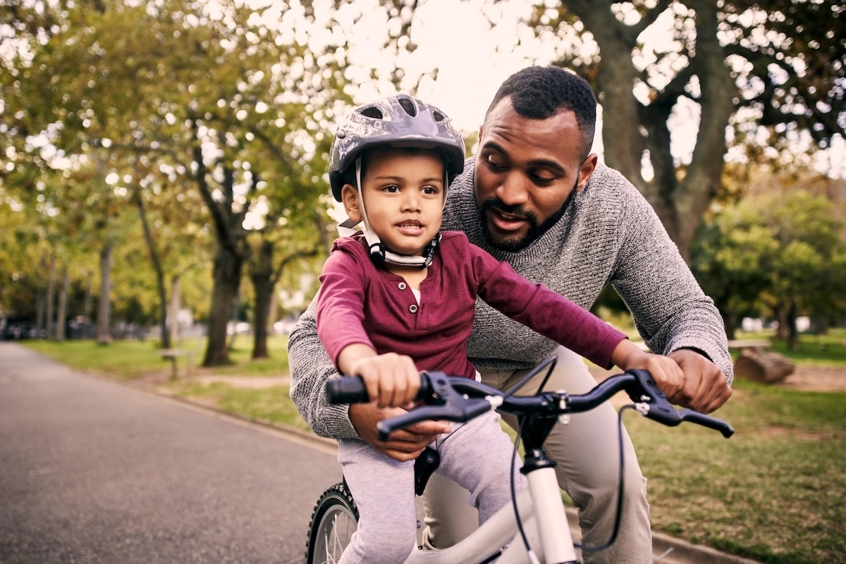 father helping child learn how to ride a bike outside